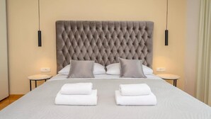 Ein Hotelzimmer mit einem gebürsteten Kopfteil, zwei Nachttischen, einem Bett mit weißer Bettwäsche und zwei Handtüchern auf dem Bett.