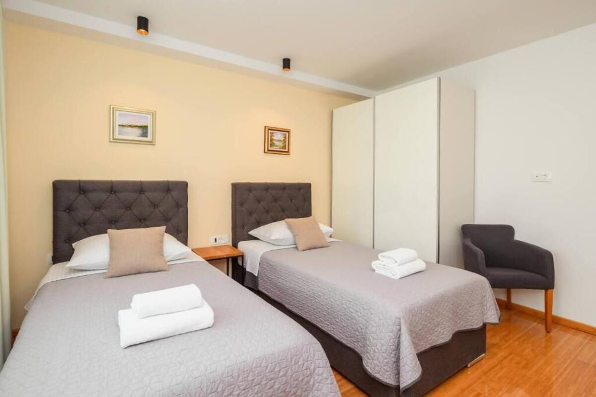 A hotel room with two beds, a chair, and a wardrobe.