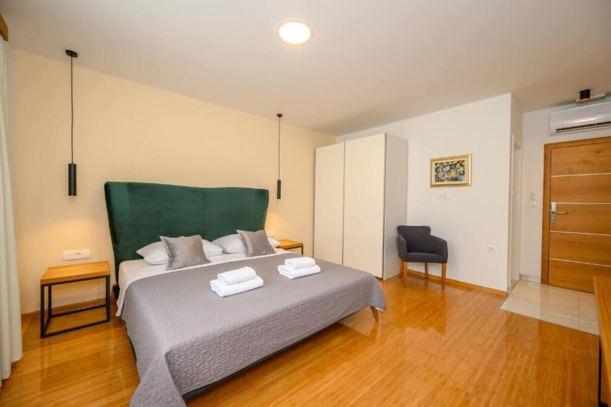A bedroom with a bed, bedside tables, a chair, an air conditioning unit, and a wardrobe.