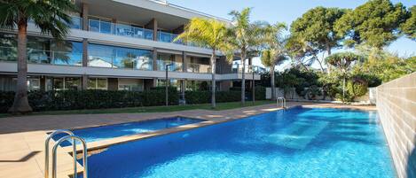 Un hotel moderno con piscina, varios balcones y abundante vegetación.