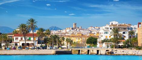 A coastal cityscape with buildings, palm trees, and a bridge over water.