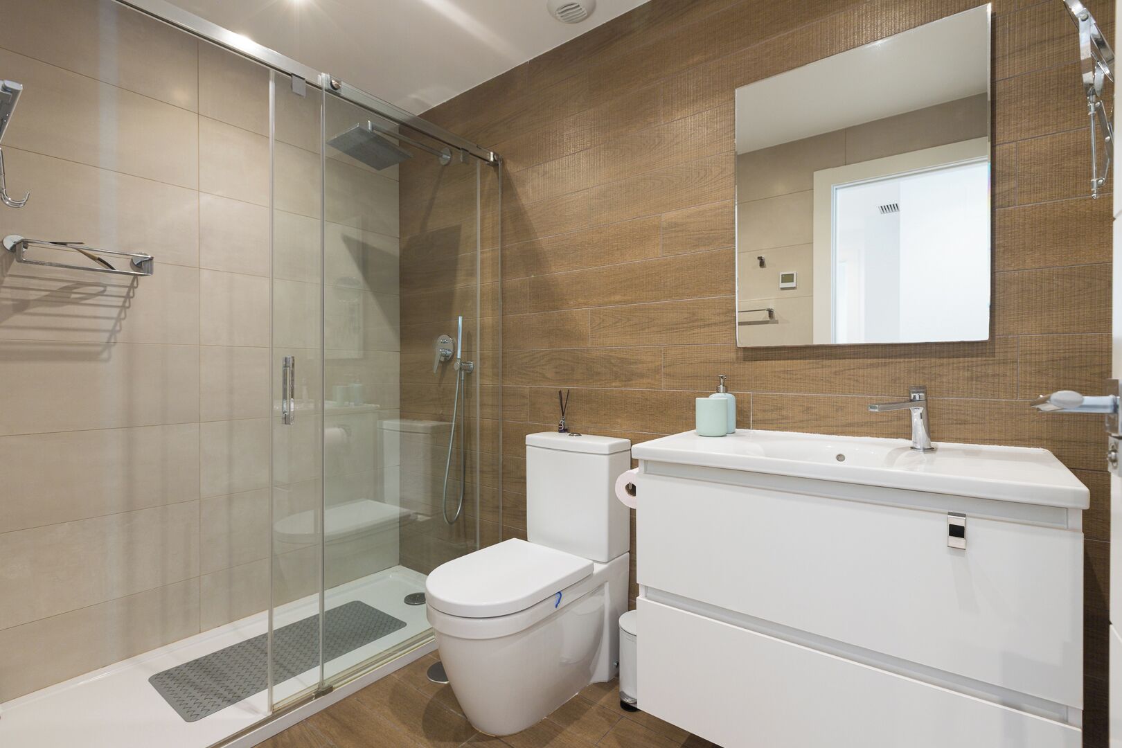 A modern bathroom with a glass-enclosed shower, a white toilet, and a sink with a mirror above.