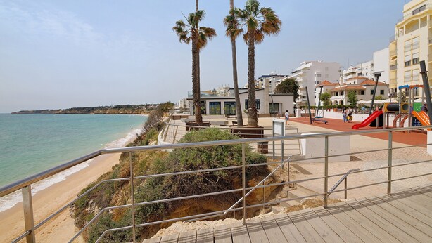 A beachside promenade with a wooden boardwalk, palm trees, and a playground. - Apt. S. Lourenço Beachfront – No Sea View, Shared Pool, Balcony & Wi-Fi (Armação de Pêra)
