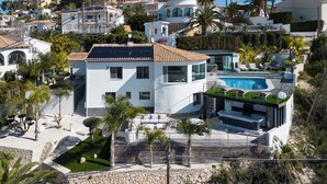 Ett modernt hus i två våningar med en swimmingpool, en terrass och utsikt över det omgivande bostadsområdet.