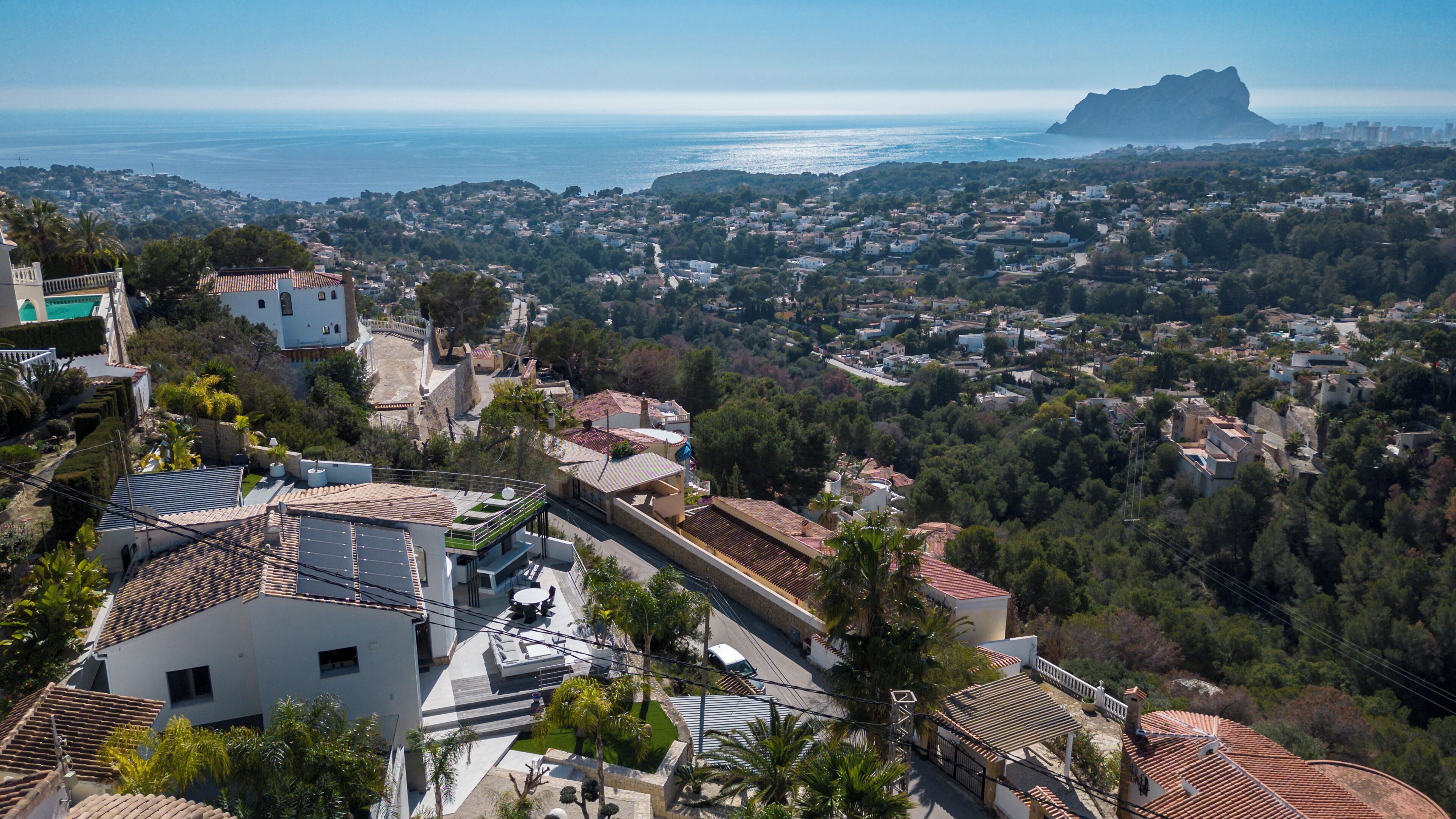 A coastal town with terraced houses, a prominent mountain in the distance, and a clear view of the sea.