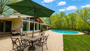 A patio with a table and chairs, a pool, and a covered area with a large umbrella.