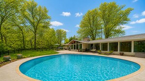 A swimming pool with a curved edge, surrounded by a patio area with outdoor furniture and a house in the background.
