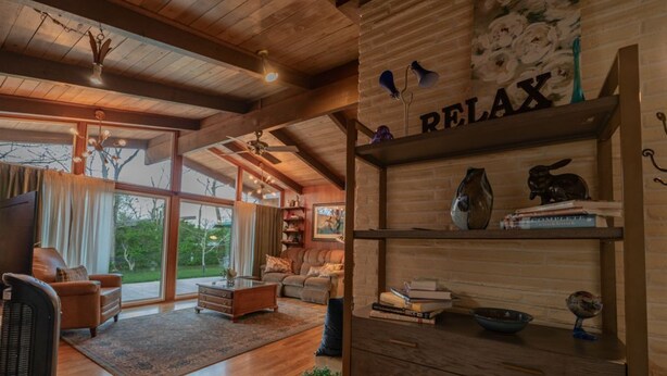 A spacious living room with wooden floors, a fireplace, a bookshelf, and a large window offering a view of the outdoors.