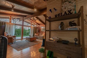 Un salon spacieux doté de planchers en bois, d’une cheminée, d’une bibliothèque et d’une grande fenêtre donnant sur l’extérieur.