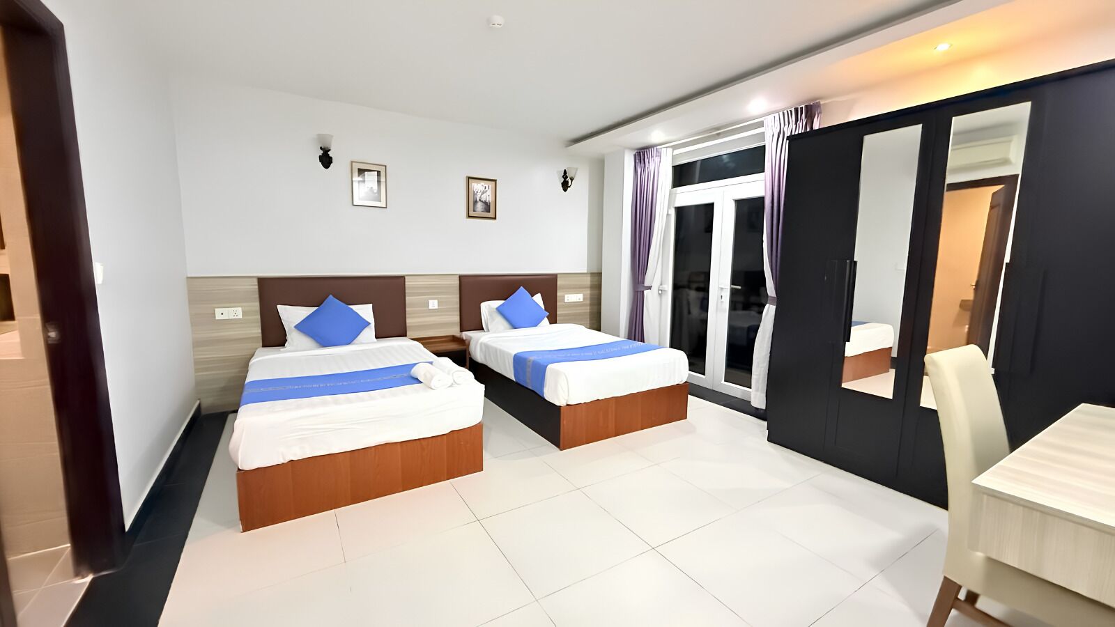 Habitación de hotel con dos camas, un escritorio y puerta corrediza a un balcón.