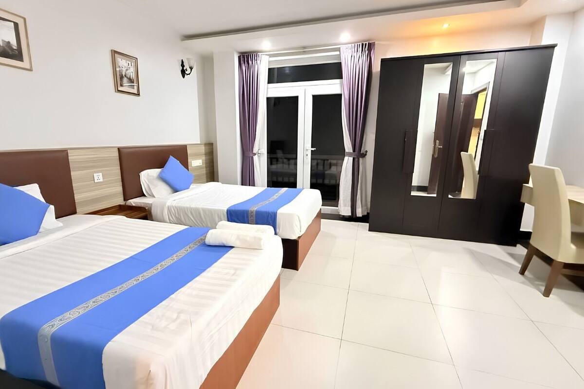 Habitación de hotel con dos camas, un escritorio y una puerta que da a un balcón.