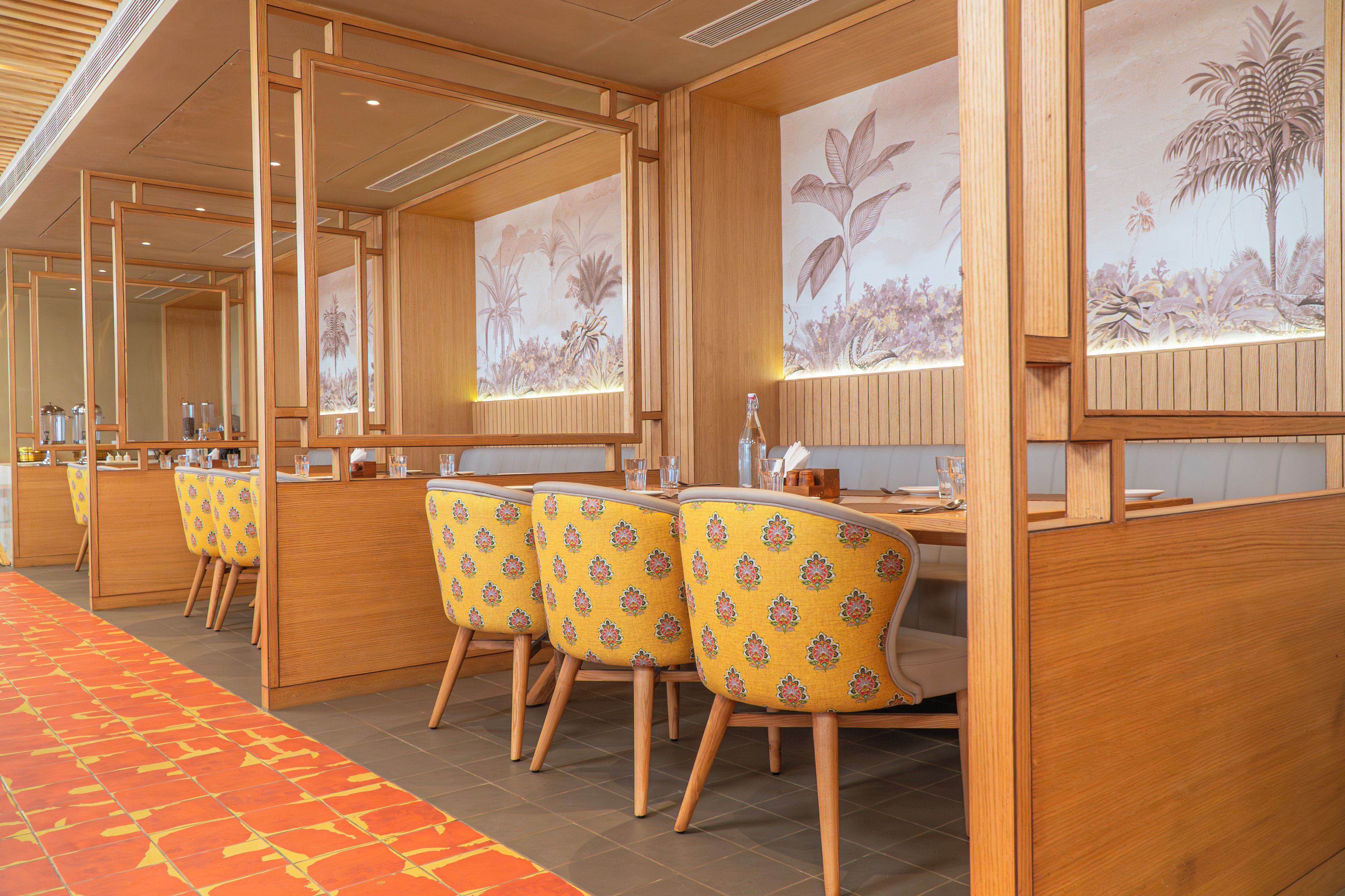 A hotel room with a wooden partition, a dining area with yellow chairs, and a carpeted floor.