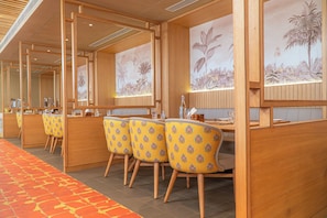 Una habitación de hotel con un separador de madera, un rincón de comedor con sillas amarillas y piso alfombrado.