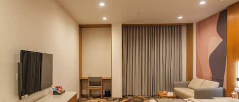 Una habitación de hotel con cama, escritorio, silla, televisión y alfombra estampada.