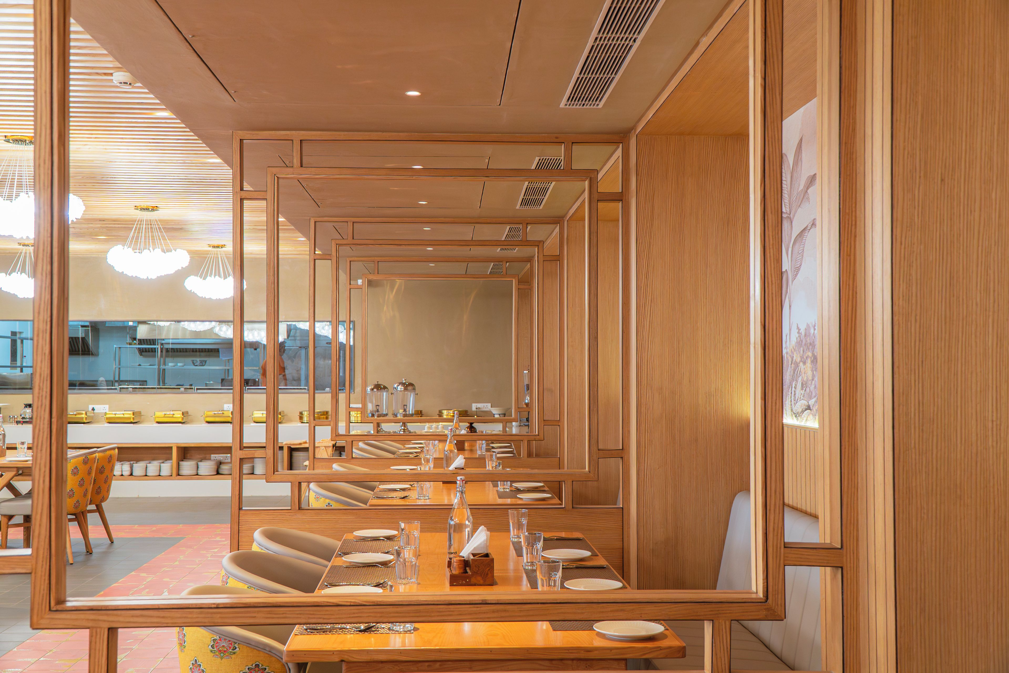 Ein Restaurant mit Spiegelwänden, Holzmöbeln und Blick auf die Küche.