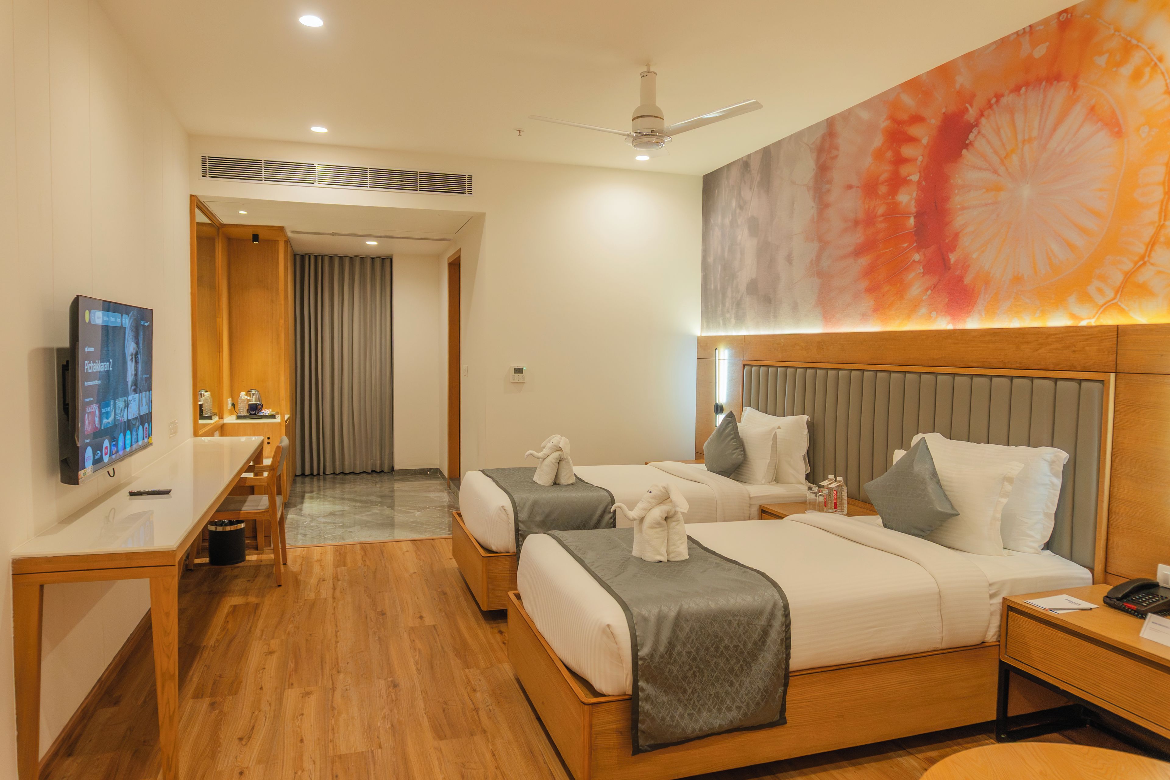 Habitación de hotel con dos camas, un escritorio, un televisor y un cuadro abstracto grande en la pared.