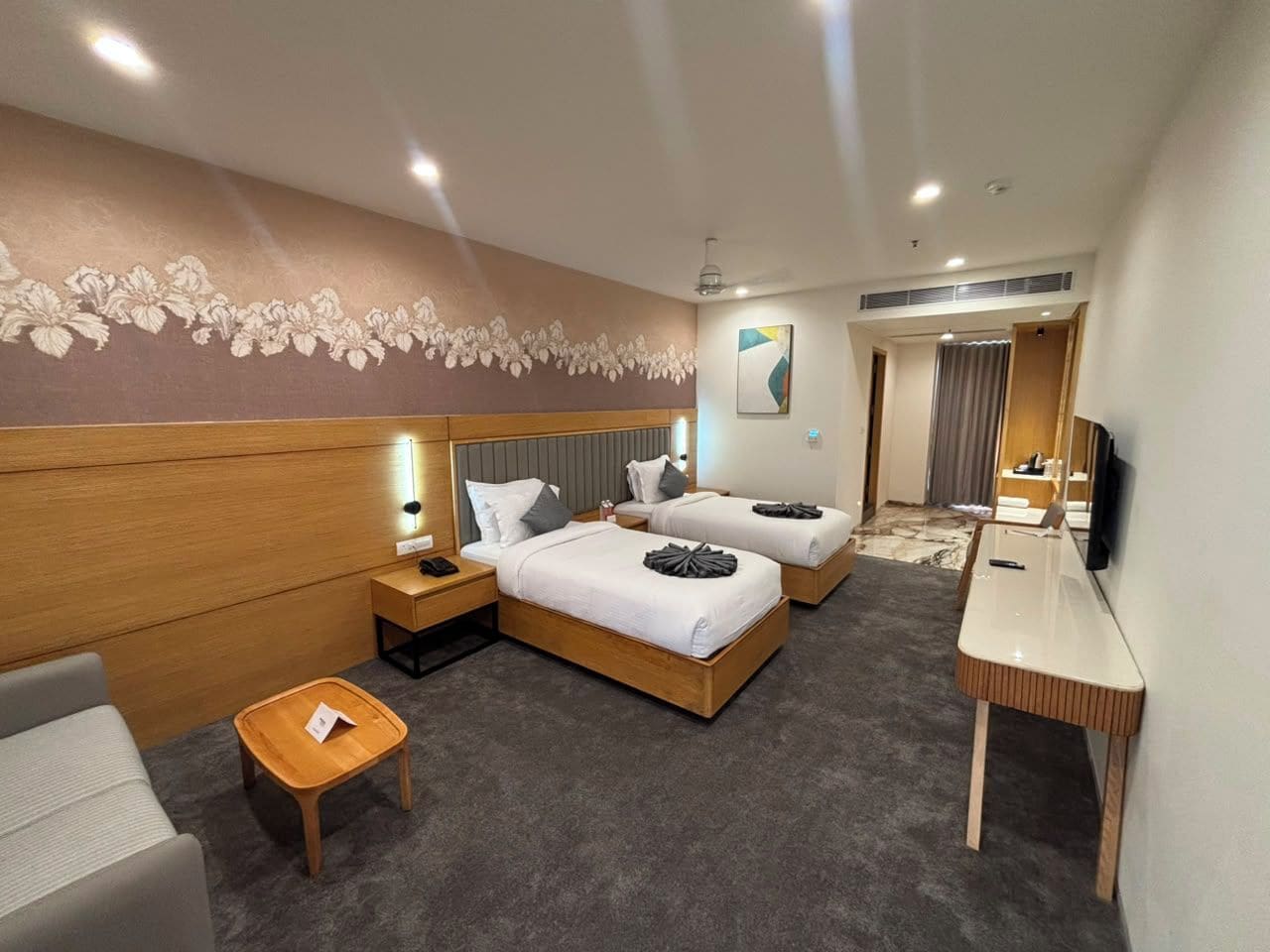 Ein Hotelzimmer mit zwei Betten, einem Schreibtisch, einem Sessel, einem kleinen Tisch und einem Fernseher.