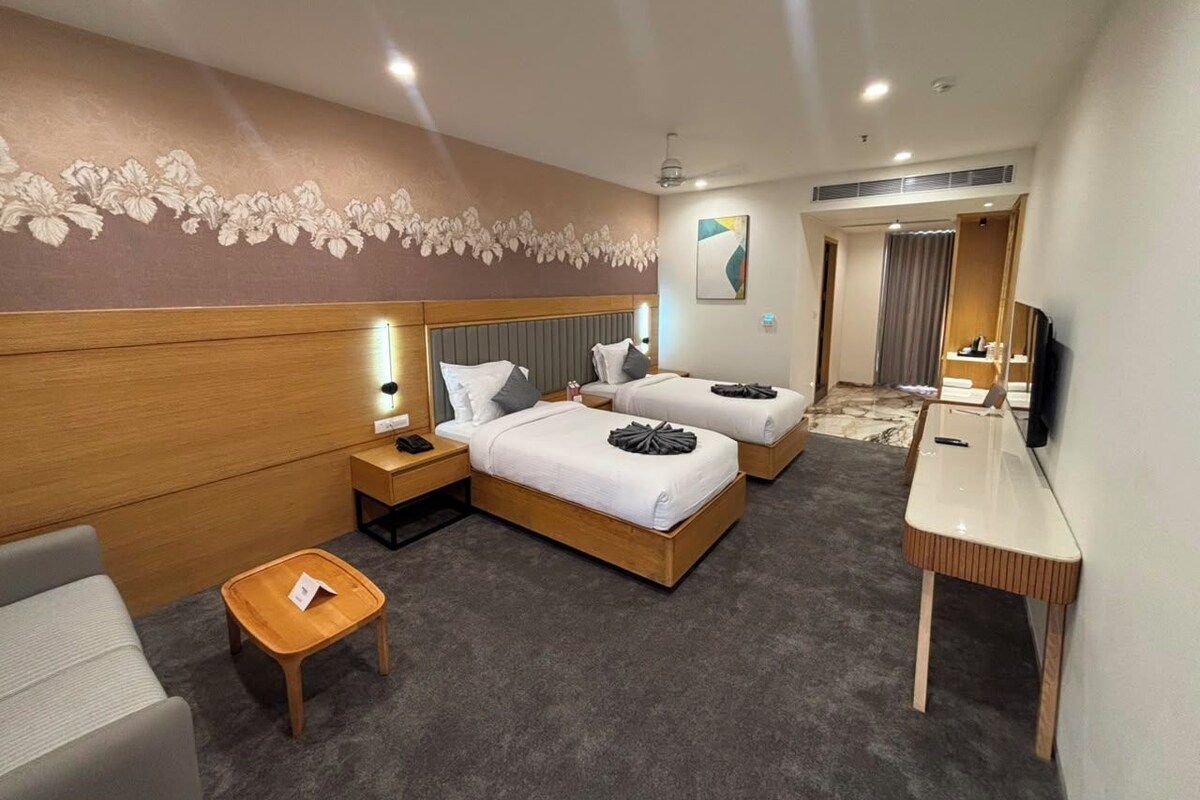 A hotel room with two beds, a desk, a chair, a small table, and a television.