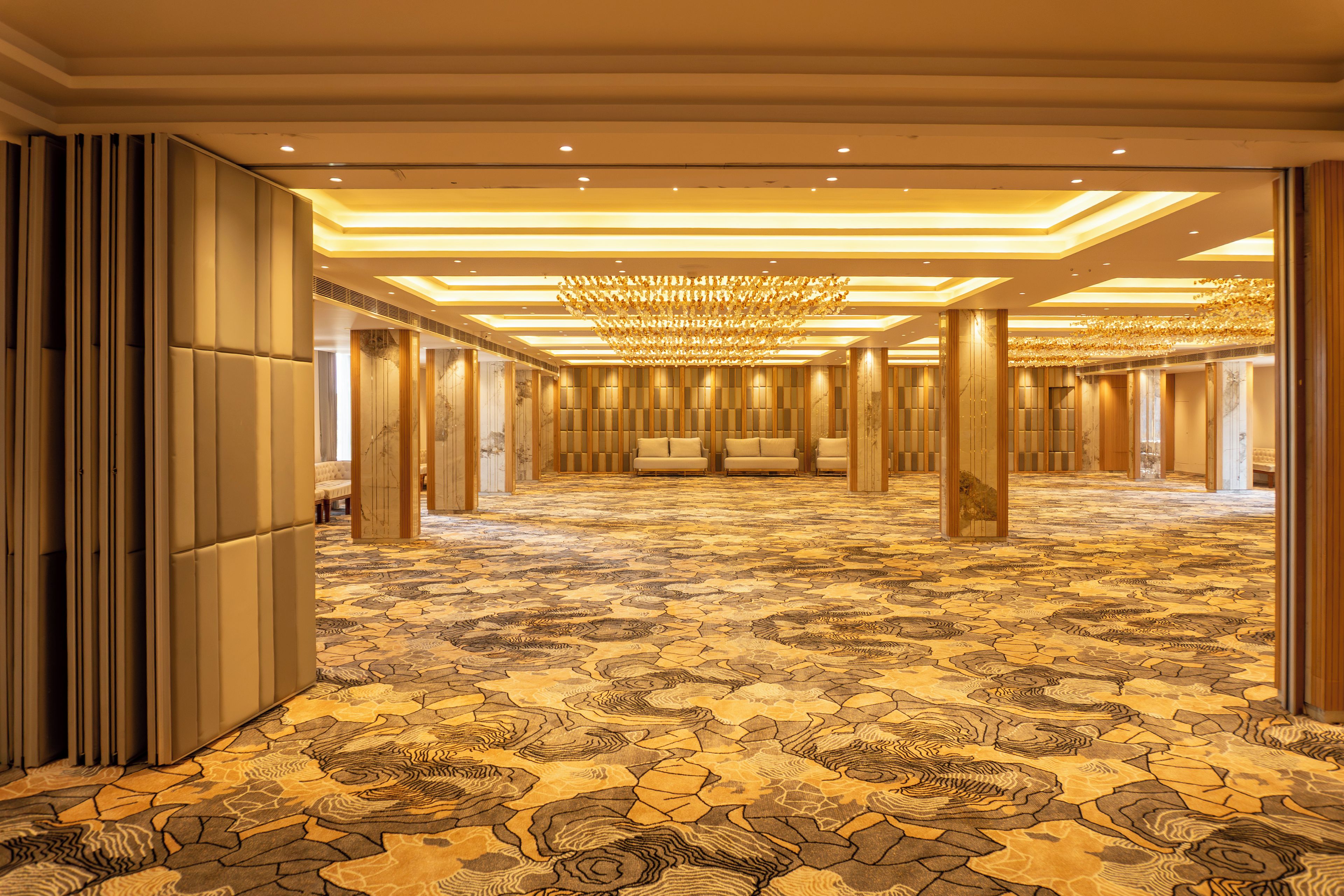 A spacious hotel lobby with a patterned carpet, a chandelier, and a row of seating.