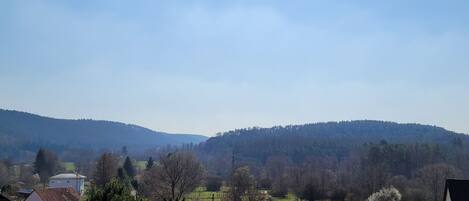 Ländliche Landschaft mit Häusern, blauem Himmel und sanften Hügeln im Hintergrund.
