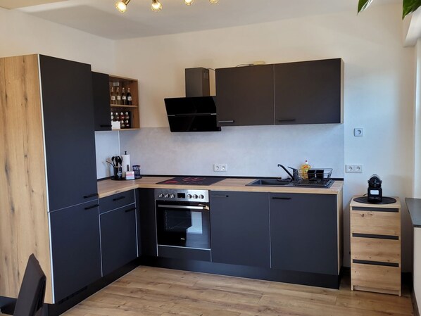 A modern kitchen with dark cabinetry, a built-in oven, and a wooden countertop.