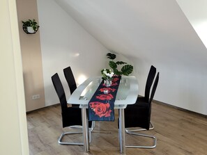 A dining table with a glass top, surrounded by black chairs, in a room with wooden flooring and a white wall. - Cozy 69-square-meter vacation apartment in the heart of the Palatinate Forest (Fischbach bei Dahn)