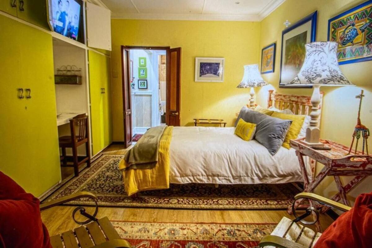 A bedroom with a bed, bedside lamps, a chair, a television, and a door leading to another room.