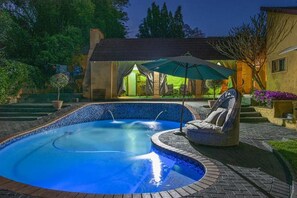 A swimming pool with a hot tub, surrounded by a brick patio, and a covered seating area with an umbrella.