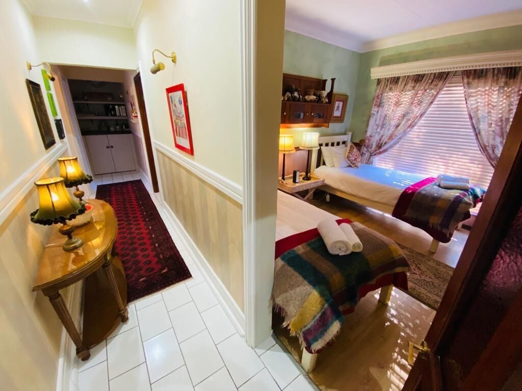 A hotel room with a bed, a bedside table with a lamp, a red rug, and a window with curtains.