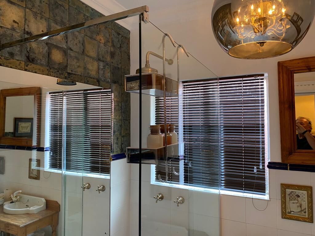 A bathroom with a glass shower enclosure, a sink, and a mirror.