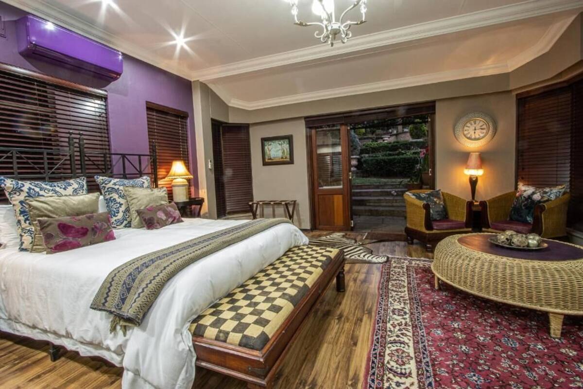A bedroom with a bed, a bench, a round wicker table, and a view of the outdoors.