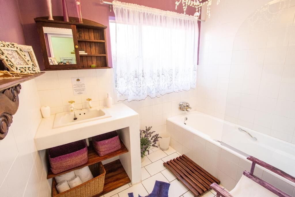 A bathroom with a white sink, a mirror, a bathtub, and a window with a white curtain.