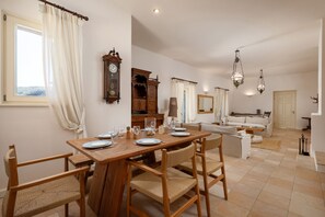 Un comedor con una mesa de madera dispuesta para cuatro personas, rodeada de sillas de mimbre. Se ve un aparador de madera y un espejo al fondo.