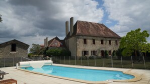 Piscina com deck de madeira, edifícios de pedra e céu nublado.