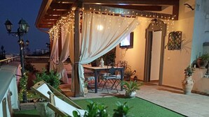 An outdoor patio with a table and chairs, string lights, and a covered seating area. - Etienne Suite (Napoli)
