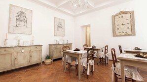 A dining area with a chandelier, antique-style wall clock, and rustic furniture. - Etienne Suite (Napoli)