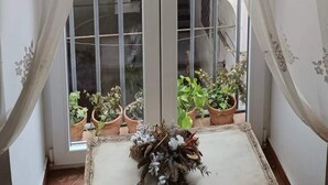 A room with a balcony, a window with sheer curtains, and potted plants. - Etienne Suite (Napoli)