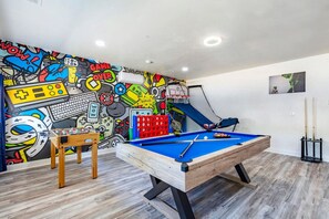 Una habitación con mesa de billar, mesa de futbolín y un mural colorido.