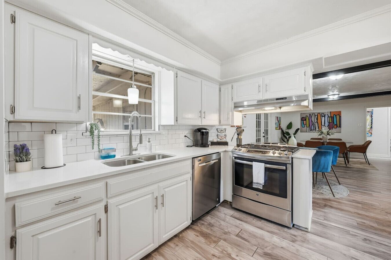 A modern kitchen with white cabinetry, stainless steel appliances, and a dining area with a round table and chairs.