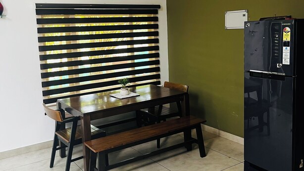 A room with a dining table, chairs, a bench, a refrigerator, a wall-mounted fan, and a window with blinds. - Hidden Serene 2BHK Villa Wayanad | Garden & Chembra Peak View (Kalpetta)