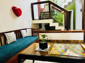 Una habitación con un sofá de madera, una mesita con un juego de mesa, una decoración con forma de corazón y una escalera.