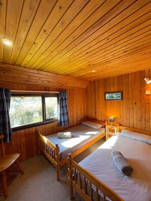 Eine Hütte mit zwei Holzbetten, einem kleinen Tisch und einem Fenster mit Vorhängen.