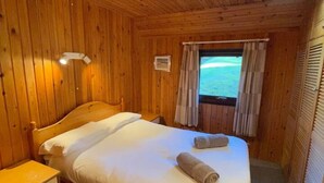 Ein Zimmer mit Holzwänden, einem Bett, einem Nachttisch und einem Fenster mit Vorhängen.