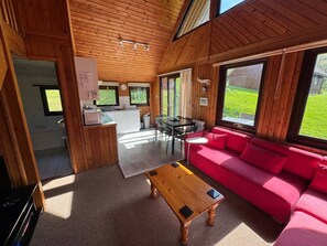 Ein gemütliches Blockhaus-Interieur mit Holzbalkendecke, einem roten Sofa, einem Esstisch und einer Küchenzeile.