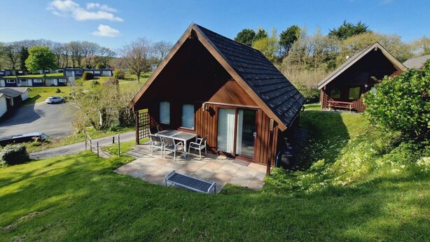 Eine Holzhütte mit Terrasse, umgeben von viel Grün und weiteren Hütten.