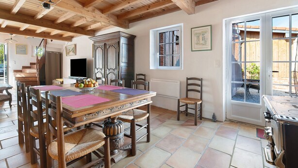 A dining area with a wooden table and chairs, a kitchen with a stove, and a window with a view of the outside. - Gîte du petit Bigot – Tranquility and Nature at the Foot of the Pyrenees (Saverdun)