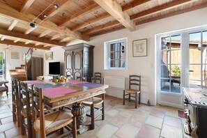Een eetgedeelte met een houten tafel en stoelen, een keuken met een fornuis, en een raam met uitzicht op buiten.