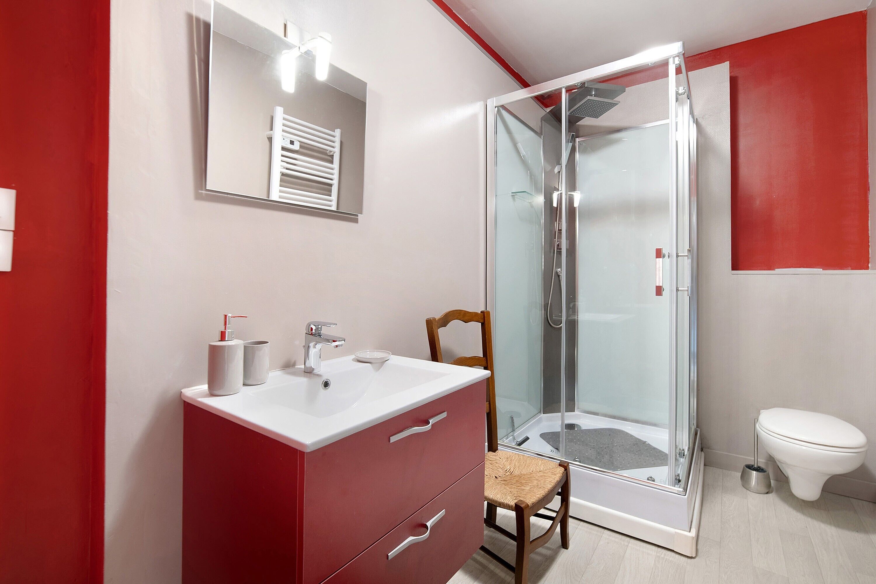 A modern bathroom with a glass shower enclosure, a white sink, and a red vanity.