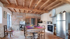 A kitchen with a brick wall, wooden ceiling beams, a stainless steel refrigerator, and a dining table with chairs. - Gîte du petit Bigot – Tranquility and Nature at the Foot of the Pyrenees (Saverdun)