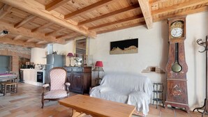 A rustic interior with a wooden ceiling, a dining area, a sofa, a bench, a large clock, and a fireplace. - Gîte du petit Bigot – Tranquility and Nature at the Foot of the Pyrenees (Saverdun)